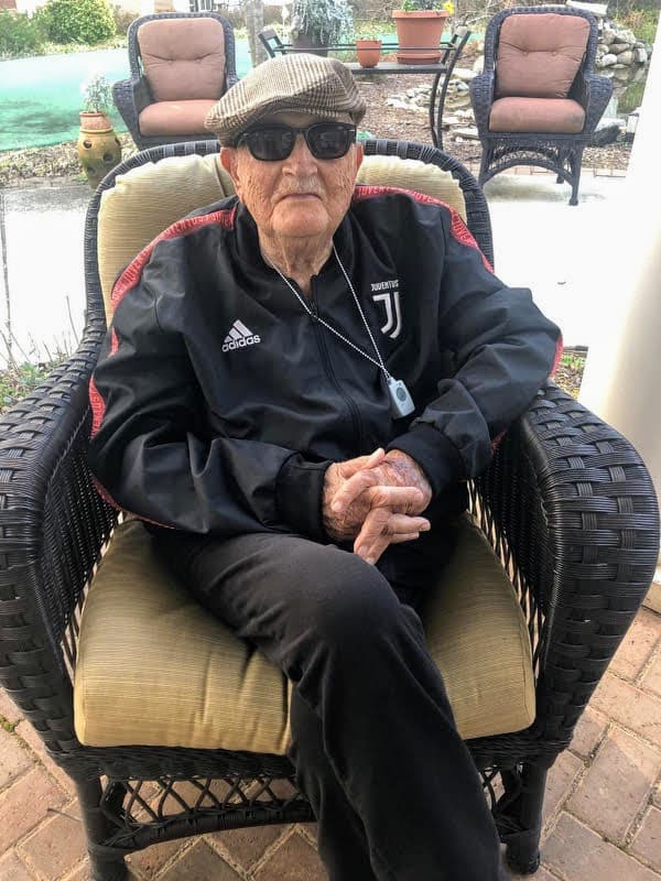 Pino Cirincione seated in a wicker chair, wearing sunglasses, a flat cap, and a Juventus track suit, hands folded