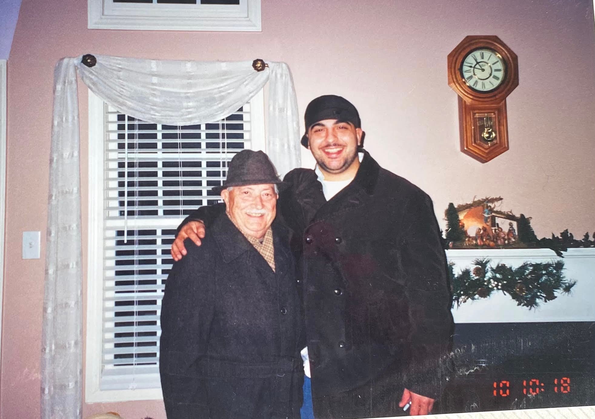 David Granado and Pino Cirincione arm in arm at a Christmas gathering, David in a do-rag, Pino in a fedora, Christmas decor in background